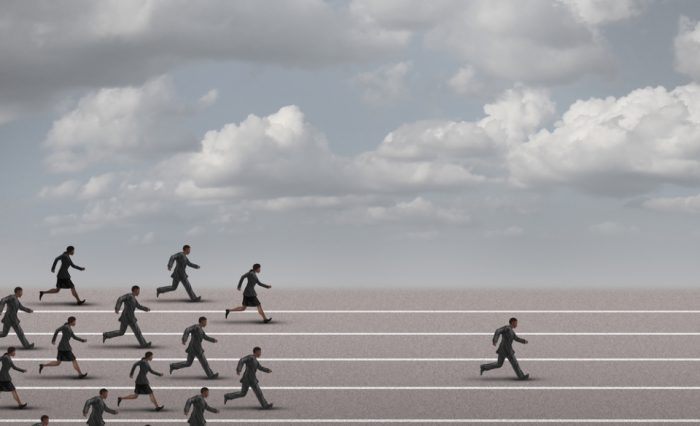 Winning the race business concept as a group of businesspeople running together with an individual businessman breaking away from the pack heading towards the finnish line as a success metaphor.